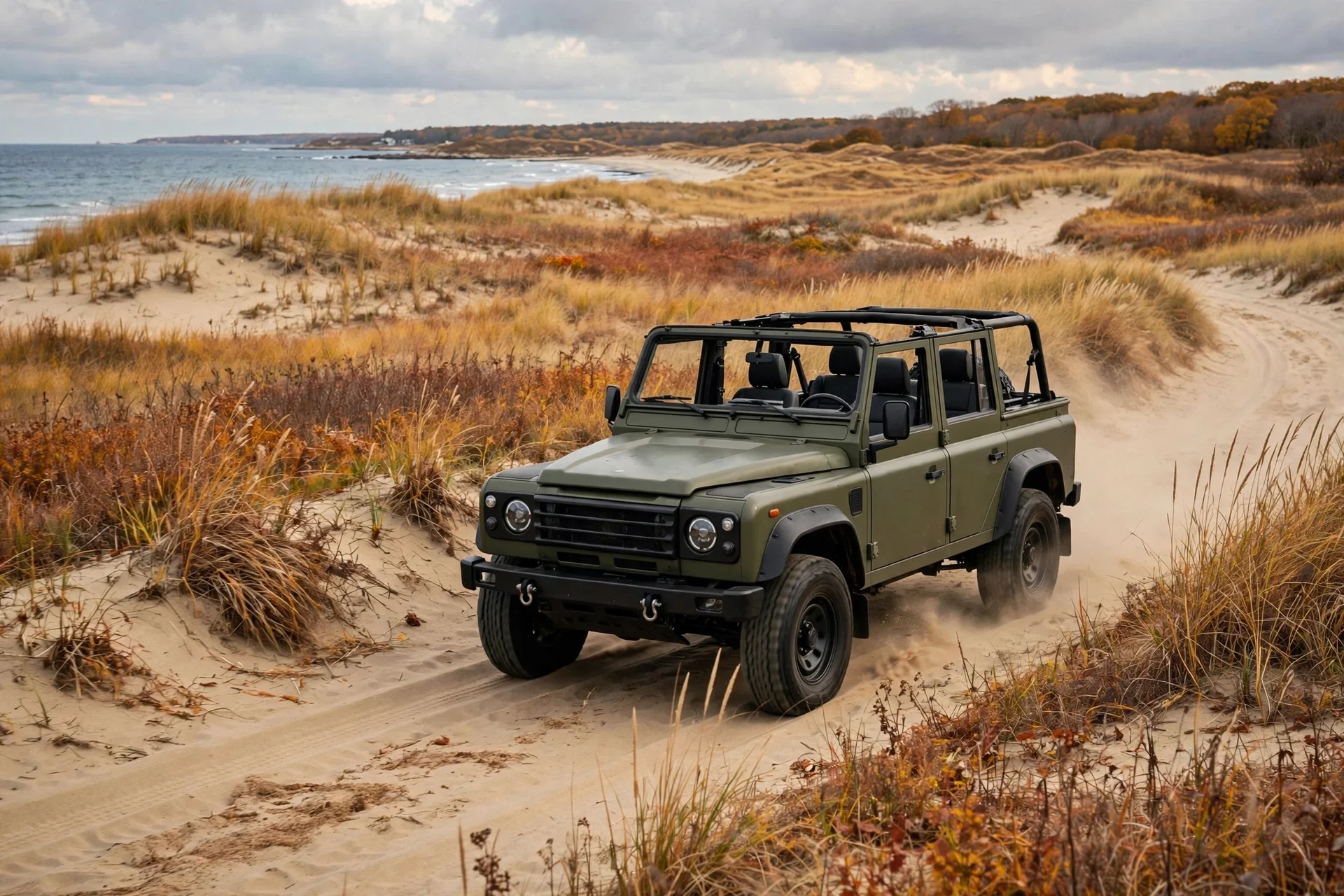 A Jeep Wrangler-style off-road SUV with its roof panels removed on a sandy coastal trail near New England dunes.